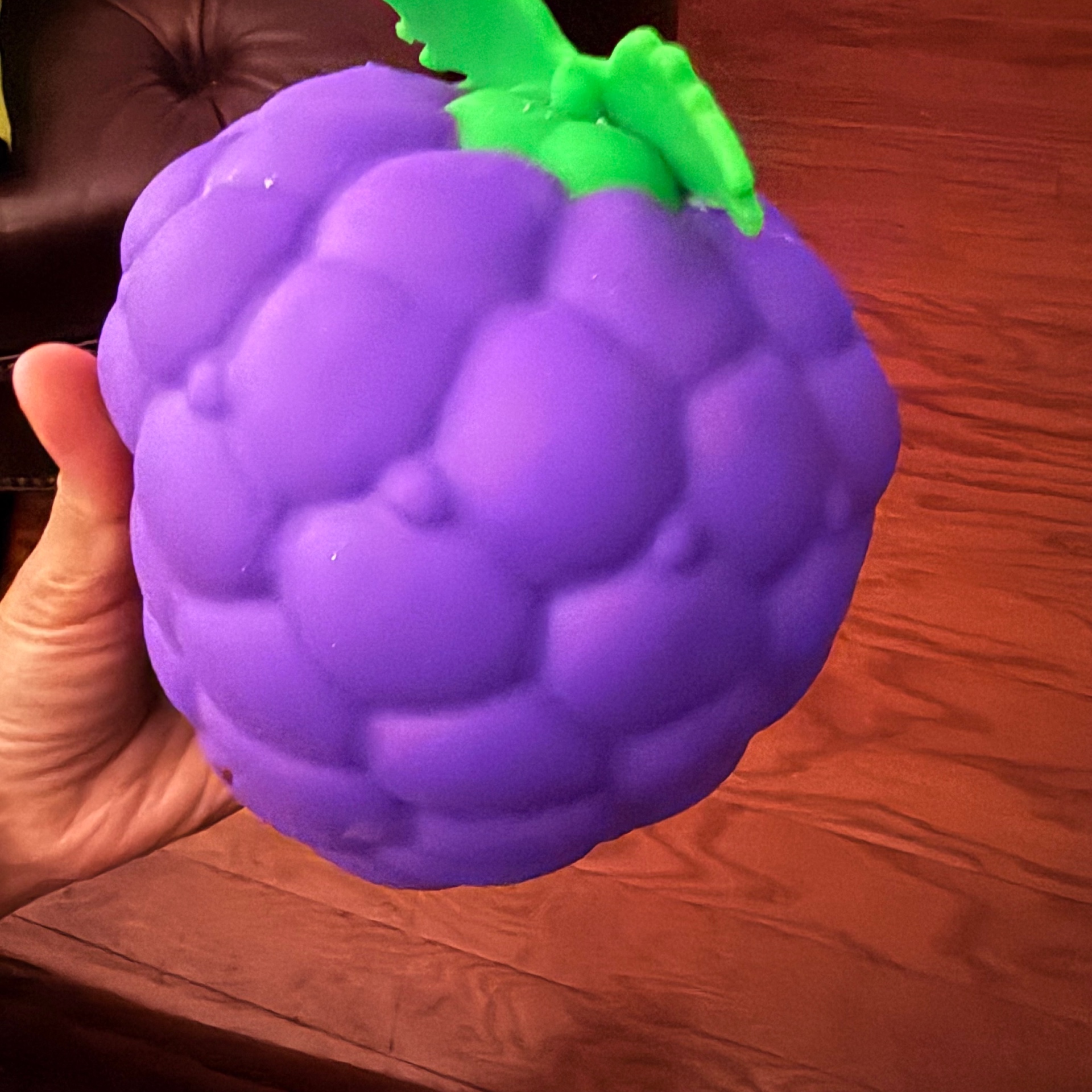 Kid's hand squeezing a giant purple grape-shaped slow-rise squishy toy with a bright green leafy stem β a Mira's Lemonade Squishy squishy review favorite
